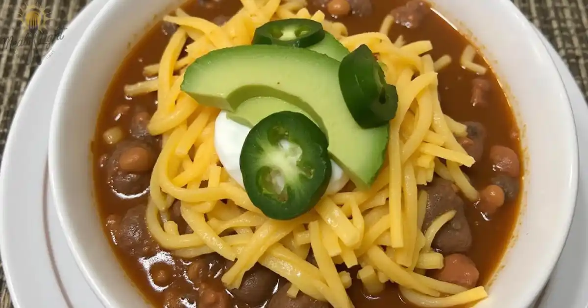 bowl of taco soup topped with shredded cheddar cheese, sliced avocado, jalapeño peppers, and a dollop of sour cream.