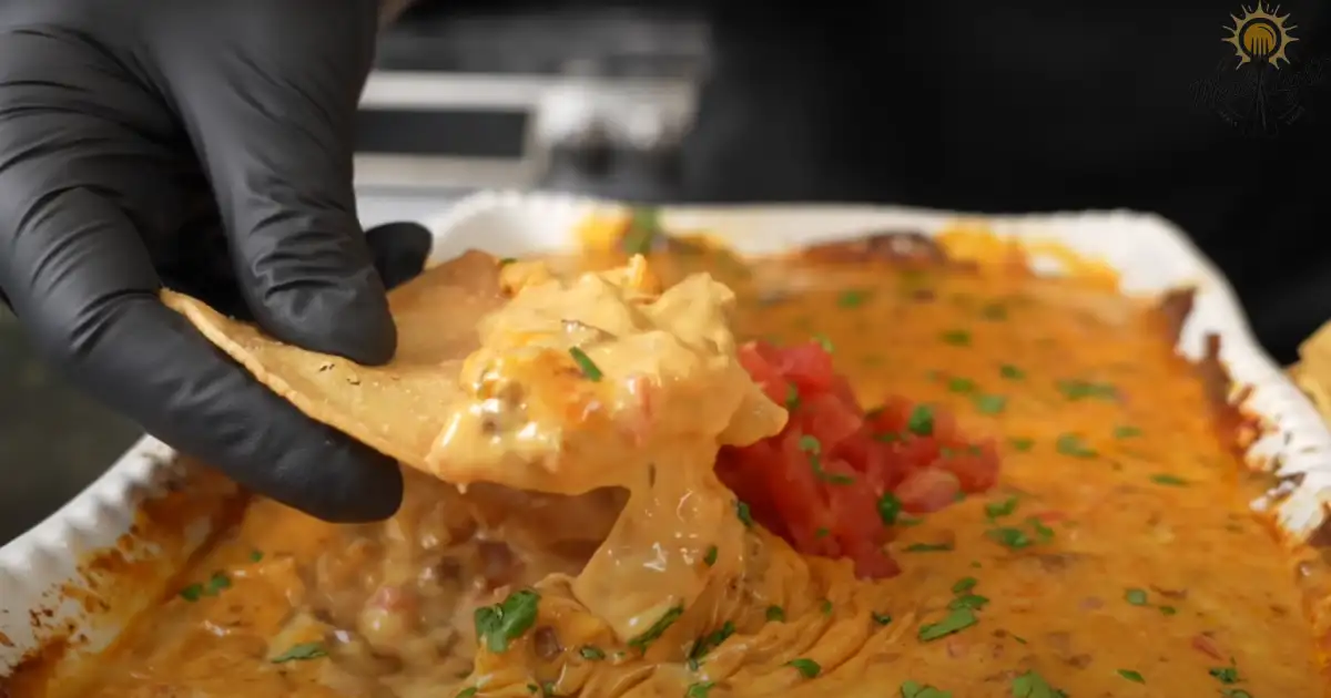 A tortilla chip dipped into a creamy, cheesy hot sausage dip, garnished with fresh tomatoes and herbs.