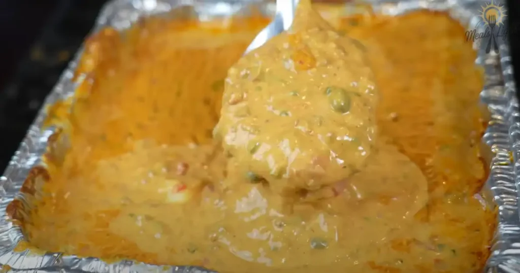 A spoonful of creamy, Hot Sausage Cheese Dip being scooped from a foil tray.