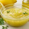 Freshly made lemon vinaigrette dressing in a glass bowl with lemons and olive oil